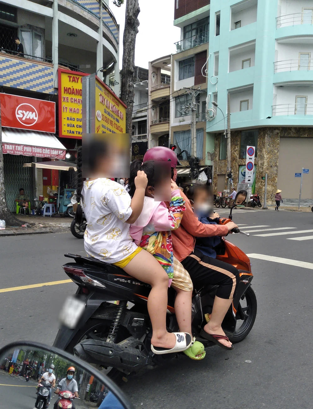 Người phụ nữ đi xe chở theo 3 trẻ em không đội mũ bảo hiểm lưu thông trên đường Nguyễn Chí Thanh, quận 5. Ảnh: THIÊN THẢO