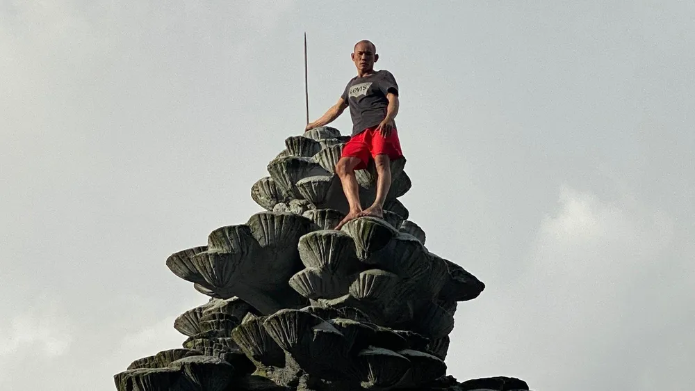 Người đàn ông đứng cheo leo trên biểu tượng quả thông trước chợ Đà Lạt. Ảnh VT