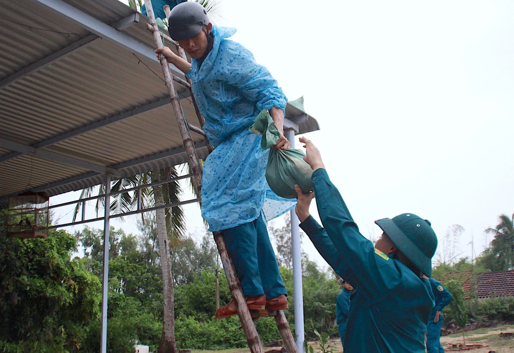 Dân quân tự vệ đưa từng bao cát lên mái chằng nhà giúp người dân.
