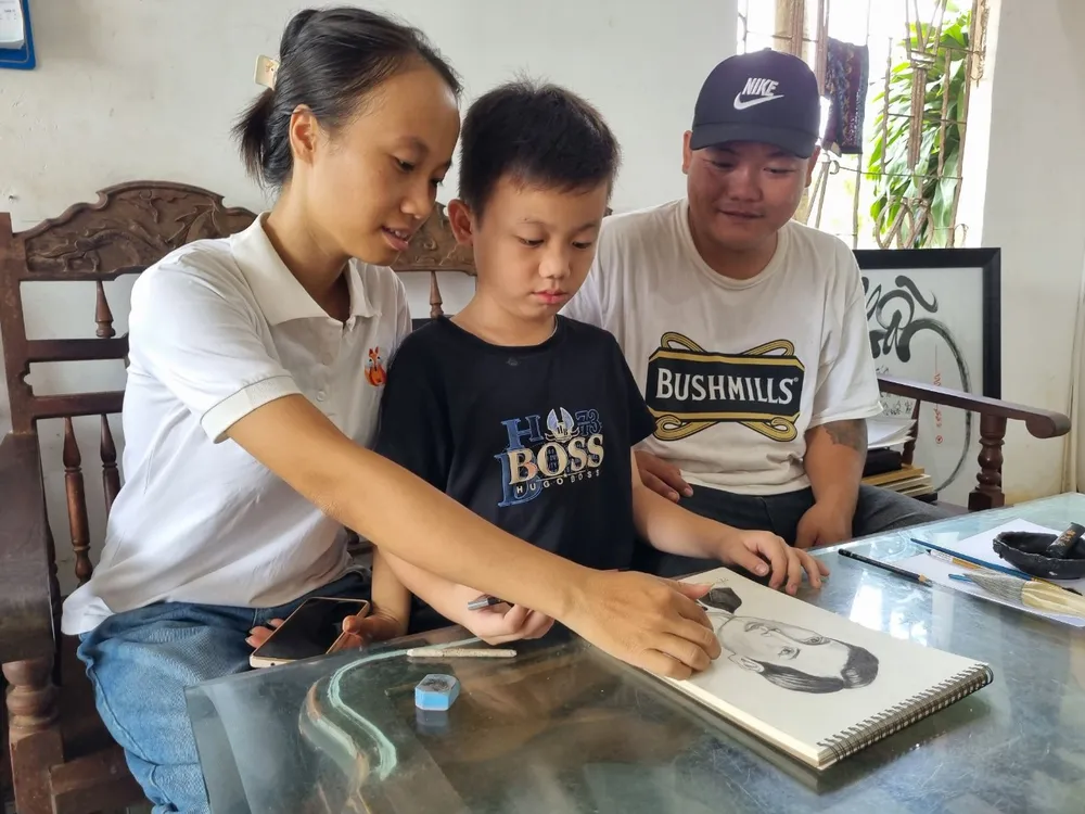 Gia đình em Nghĩa cùng xem lại bức vẽ chân dung Chủ tịch Hồ Chí Minh thời trẻ. Ảnh: TIẾN THOẠI vẽ tranh 8.jpg
