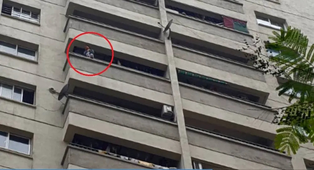 Cháu bé ngồi vắt vẻo trên ban công tầng 12 (Ảnh cắt từ clip của anh Nguyễn Hà).