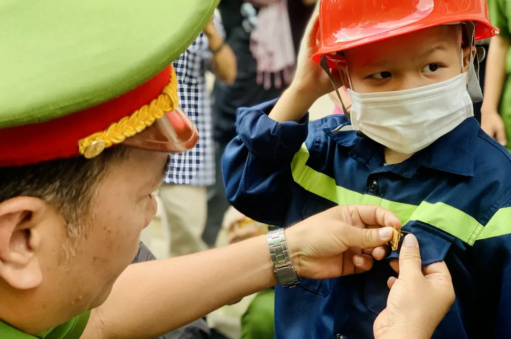 Thượng tá Nguyễn Thanh Tùng đeo biểu tượng huy hiệu của lính cứu hỏa cho Quân. Ảnh: THẢO PHƯƠNG