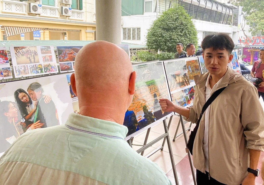 Một du khách nước ngoài nghe giới thiệu về các bức ảnh. Ảnh: VIẾT THỊNH. nguoi-mat-chong-va-2-con-bat-khoc-tai-trien-lam-vuon-len-thon-lang-nu-3.JPEG