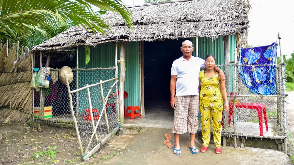 Vợ chồng ông Việt bên căn nhà lợp lá, cất trên nền đất mượn của người thân. Ảnh: MINH TRUNG