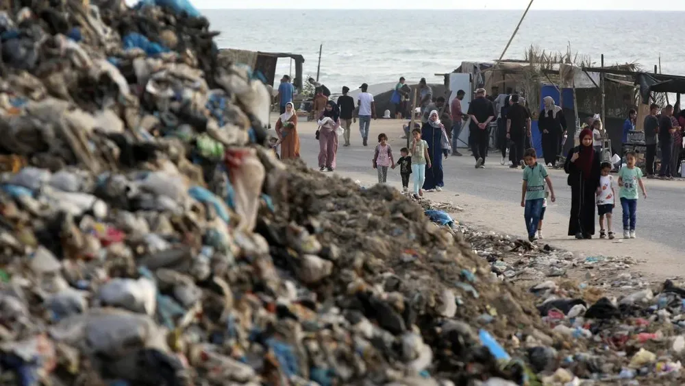Người dân đi ngang bãi rác ở Deir al Balah (miền trung Gaza) vào tháng 5. Ảnh: ANADOLU AGENCY Cuộc xung đột ở Gaza