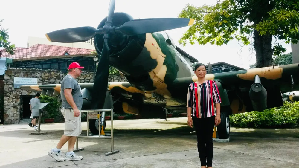 Chị Nguyệt chụp hình lưu niệm với hiện vật trong khuôn viên bảo tàng. Ảnh: PHƯƠNG LÊ.