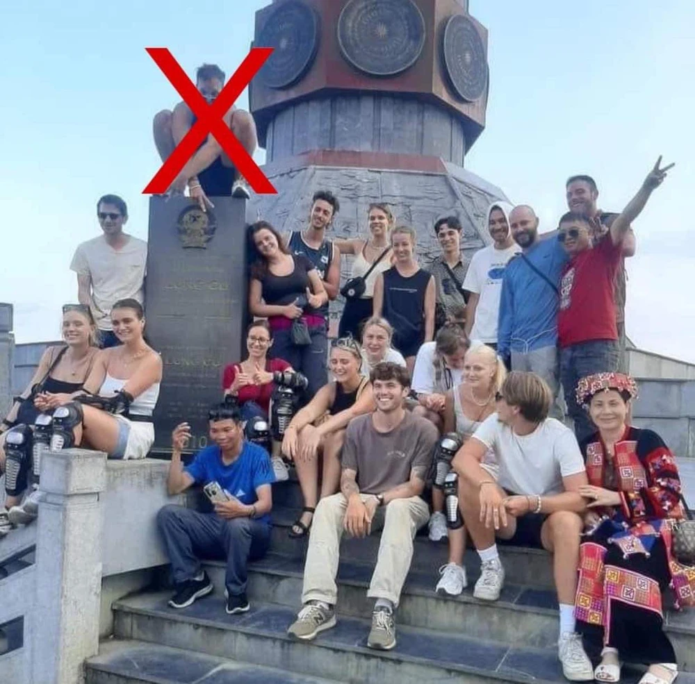 Một vị khách người nước ngoài ngồi trên tấm bia có khắc hình quốc huy và thông tin điểm cột cờ Lũng Cú. Ảnh: Mạng xã hội.