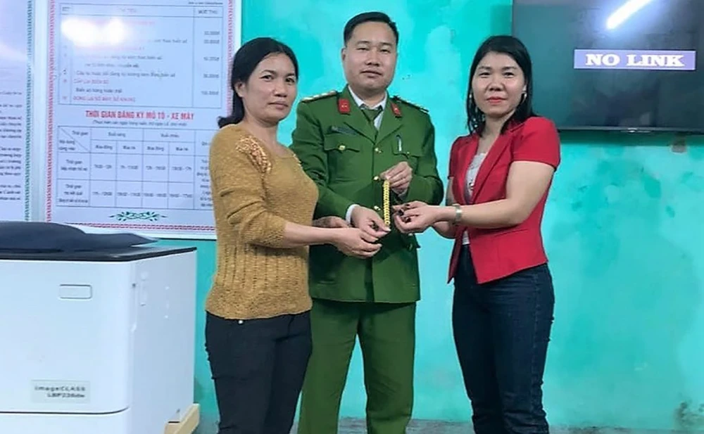 Cô giáo Lê Thị Minh (áo đỏ) cùng công an trả lại sợi dây chuyền vàng cho người đánh rơi. Ảnh: CATX