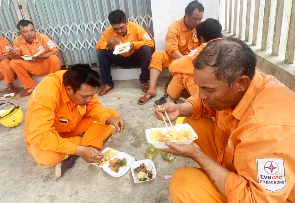 Công nhân PC Đắk Nông tranh thủ ăn cơm hộp tại hiện trường cố gắng khắc phục sự cố, cấp điện trở lại sớm nhất phục vụ người dân. Ảnh: BM