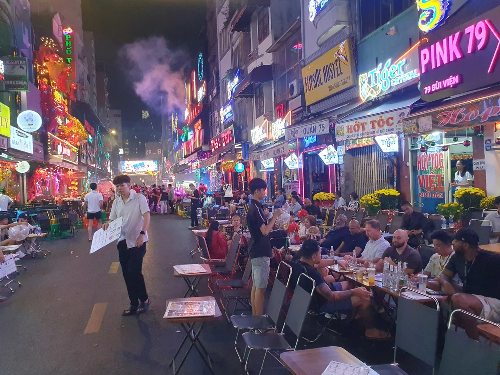 Một số nhóm du khách người nước ngoài quây quần bên nhau chờ đón thời khắc năm mới. Phía ngoài, nam nhân viên của quán liên tục mời gọi khách vào quán mình.