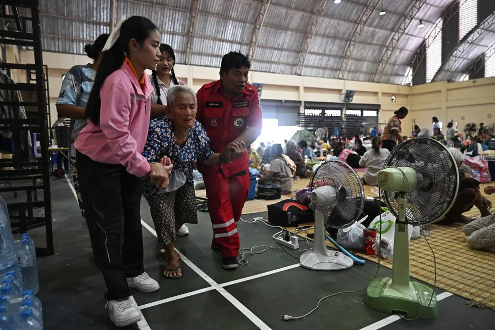 Một cụ già được hỗ trợ khi trú ẩn trong nhà thi đấu ĐH Rajabhat Surindra, tỉnh biên giới Surin, Thái Lan. Ảnh: Lillian Suwanrumpha/AFP