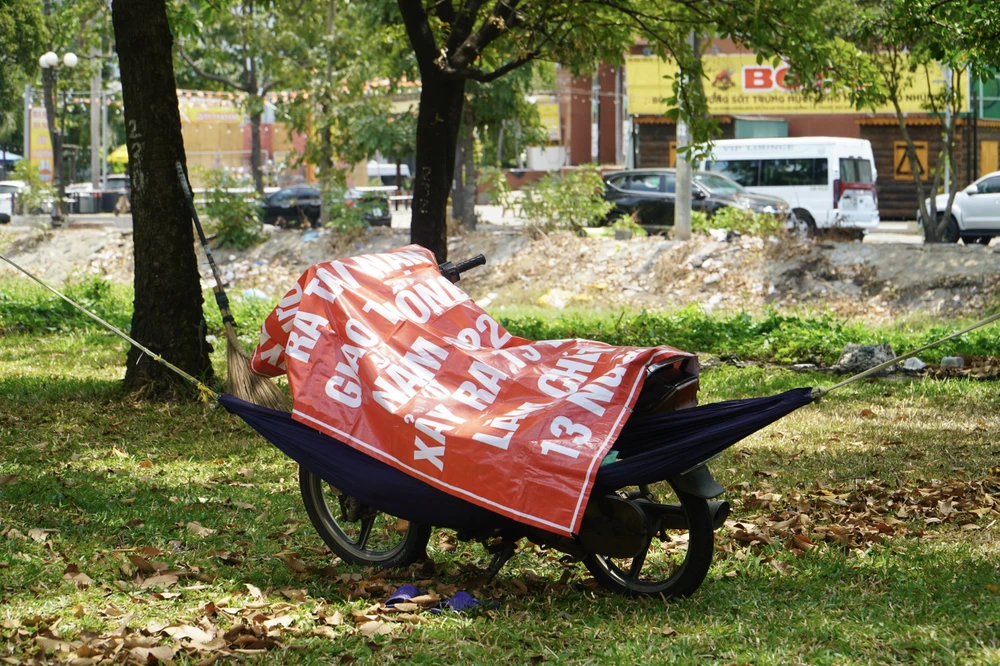 Một người tận dụng tấm bạt cũ để che nắng. Ảnh: HUỲNH THƠ