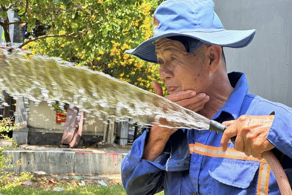 Chú Sáu, một công nhân tưới nước công viên tranh thủ lúc làm việc dùng nước rửa mặt để mát mẻ hơn. Ảnh: HUỲNH THƠ