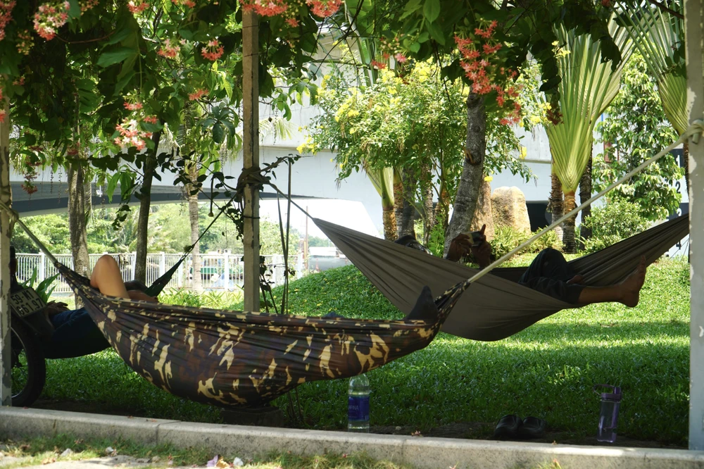 Một một bình nước lớn cùng một cái võng dưới bóng cây là giải pháp tránh nắng của các công nhân giờ nghỉ trưa. Ảnh: HUỲNH THƠ