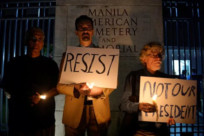 Các công dân Mỹ biểu tình phản đối ông Trump tại Manila (Philippines) tối 20-1. Ảnh: REUTERS