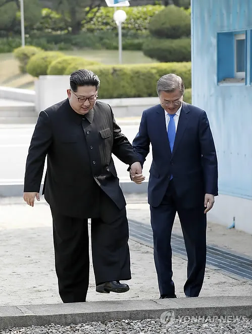Lãnh đạo Triều Tiên Kim Jong-un (trái) và Tổng thống Hàn Quốc Moon Jae-in cùng nắm tay bước lại sang phần đất Hàn Quốc sau khi bước sang phần đất Triều Tiên, lại làng đình chiến Bàn Môn Điếm sáng 27-4. Ảnh: YONHAP