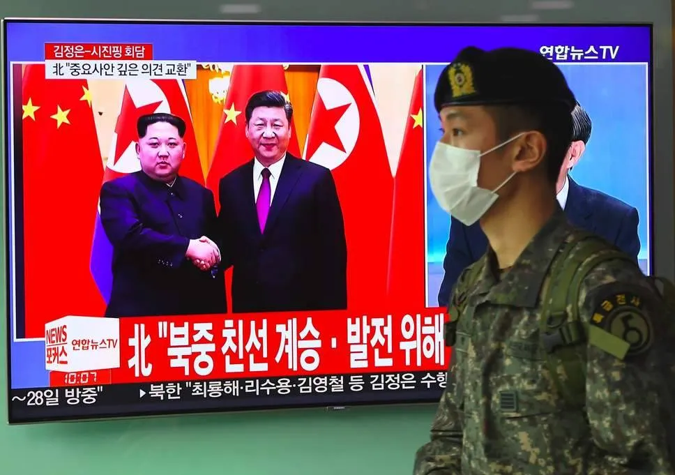 Một binh sĩ Hàn Quốc bước qua màn hình ti vi đang đưa tin về chuyến thăm Bắc Kinh của lãnh đạo Triều Tiên Kim Jong-un và gặp Chủ tịch Trung Quốc Tập Cận Bình ngày 28-3. Ảnh: AFP