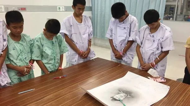 Các cậu bé cúi đầu tưởng niệm thợ lặn Saman Kunan, cựu đặc nhiệm hải quân Thái Lan thiệt mạng vì thiếu ô xy trong quá trình lặn lắp đặt bình ô xy dọc hang động chuẩn bị cho công tác giải cứu. Ảnh: AP