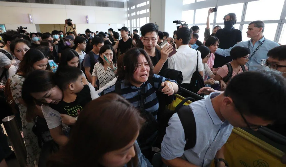 Hành khách bật khóc trong khi cố len lỏi qua đám đông tại sân bay. Ảnh: SCMP