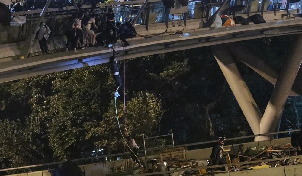Người biểu tình đu dây từ cây cầu đi bộ xuống con đường bên dưới thoát ra khỏi trường, khuya 18-11. Ảnh: SCMP