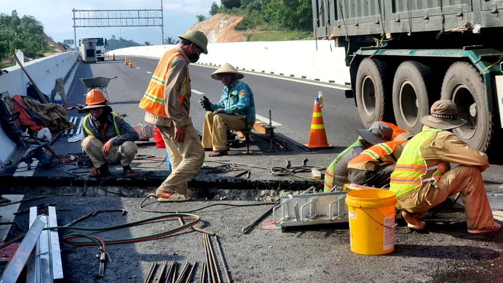 Các công nhân thi công bên dòng phương tiện lưu thông với tốc độ cao. Công nhân cho biết đang lắp các khe co giãn trên cao tốc.