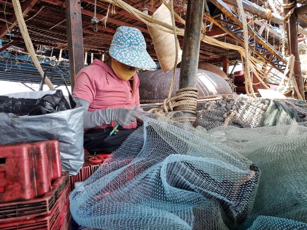 Vợ ngư dân vá lưới chờ ngày giá xăng dầu giảm để ra khơi. Ảnh: THANH NHẬT.