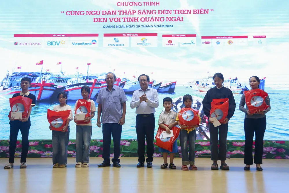 Ông Trương Hòa Bình, Nguyên Ủy viên Bộ Chính Trị, Nguyên Phó Thủ tướng Thường trực Chính phủ và ông Mai Ngọc Phước, Tổng Biên tập báo Pháp Luật TP.HCM, trao học bổng cho các em học sinh. dang-dien-ra-chuong-trinh-cung-ngu-dan-thap-sang-den-tren-bien-tai-quang-ngai-2.jpg