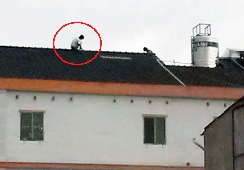 Tên trộm cố thủ trên nóc nhà, dọ sẽ nhảy xuống tự tự nếu ai đó tiếp cận bắt. Ảnh: Độc giả cung cấp