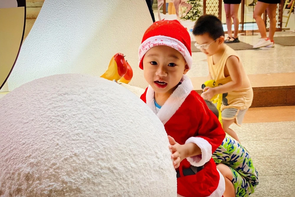 Một em nhỏ mặc đồ ông già Noel hớn hở chụp ảnh cùng người tuyết. Ảnh: TÚ NGÂN