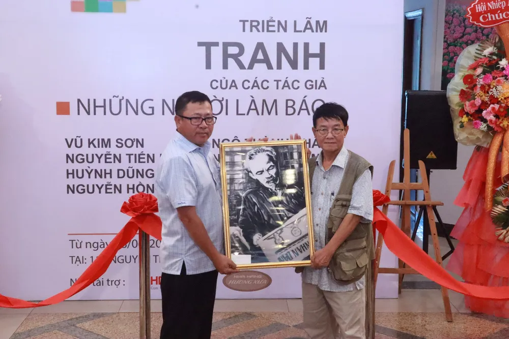 Nhà báo Huỳnh Dũng Nhân tặng bức chân dung Chủ tịch Hồ Chí Minh đọc báo cho đại diện báo Nhân Dân. trien-lam-tranh5.png