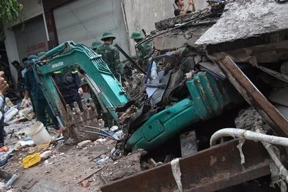 Một chiếc xe cẩu bị khối bê tông đè bẹp ngay dưới chân tòa nhà.