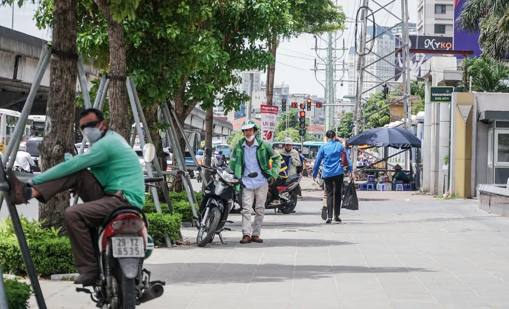 Trên đường Phạm Hùng, những tài xế xe ôm cố tìm chút bóng mát từ tán cây để chờ khách, tranh thủ nghỉ ngơi.