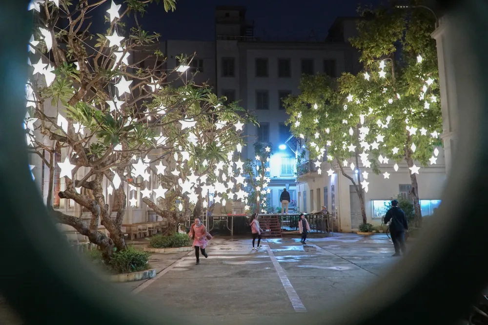 Trong khoảng sân lớn, những chiếc đèn hình ngôi sao được mắc khắc trên hàng cây xanh tỏa ánh sáng rực rỡ. Trong khoảng sân lớn, những chiếc đèn hình ngôi sao được mắc khắc trên hàng cây xanh tỏa ánh sáng rực rỡ.