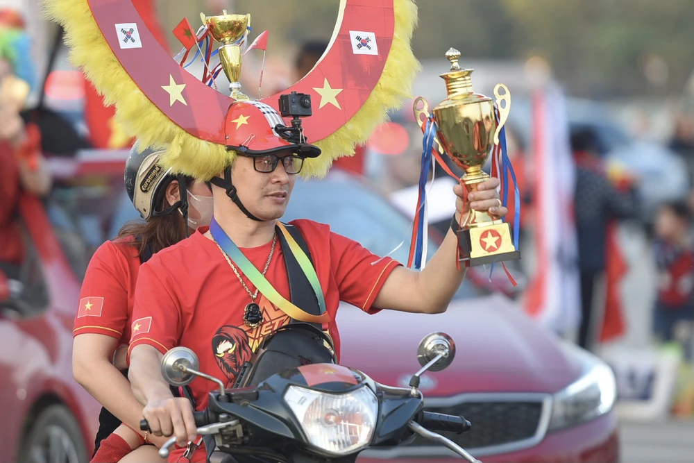 Chiếc cúp và trang phục rực rỡ, vui nhộn của cổ động viên khu vực trước sân Mỹ Đình. Chiếc cúp và trang phục rực rỡ, vui nhộn của cổ động viên khu vực trước sân Mỹ Đình.