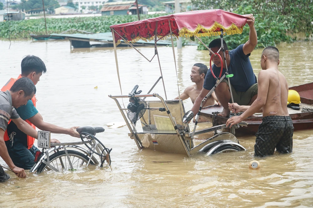 Khu vực này vốn là bãi đỗ xe, nhưng chỉ sau một đêm, nước sông Hồng đã dâng lên nhấn chìm mọi thứ. Anh chủ xích lô phải lặn ngụp mãi, hơn một giờ mới kéo được phương tiện 'kiếm cơm' lên chỗ cao hơn.