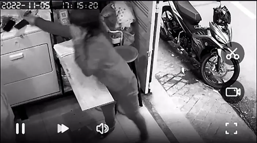 Người phụ nữ với tay lấy điện thoại của nhân viên. Ảnh cắt từ clip Người phụ nữ với tay lấy điện thoại của nhân viên. Ảnh cắt từ clip