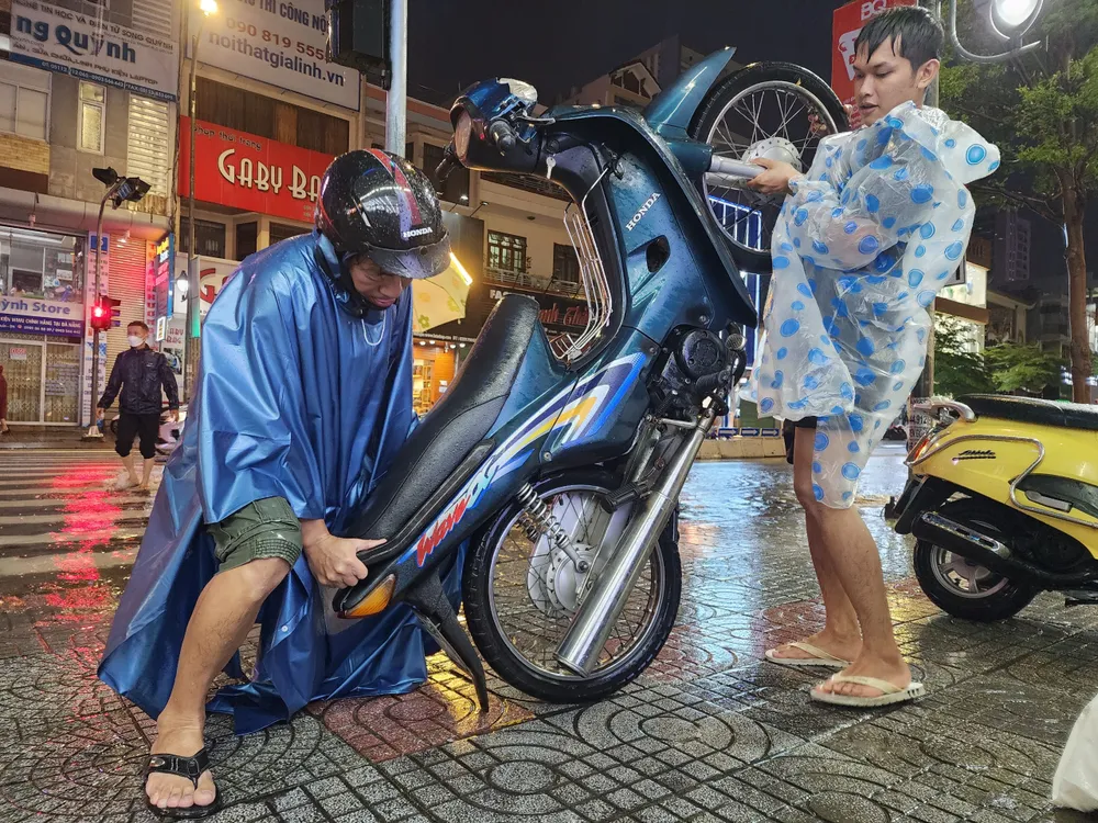 Tuyến đường Lê Duẩn, hai bố con dựng đứng xe máy để dốc hết nước trong ống xả ra ngoài nhằm cứu xe. Ảnh: MINH TRƯỜNG. hai bo con dung xe may da nang ngap nuoc.jpg