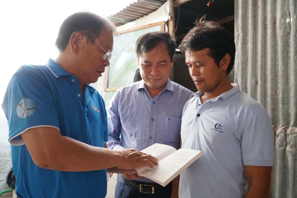 Phó Trưởng Ban Tuyên giáo Trung ương Phan Xuân Thủy (giữa) cùng Tổng biên tập báo Pháp Luật TP.HCM Mai Ngọc Phước thăm hỏi ngư dân Nguyễn Văn Công và giới thiệu nội dung cuốn cẩm nang &quot;Những điều cần biết khi đánh bắt hải sản&quot;. Ảnh: NHẬT DIỄM