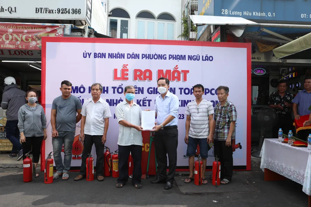 Ông Lê Tấn Đạt, Bí thư Đảng ủy Phường Phạm Ngũ Lão (mặc áo trắng, đứng thứ 3 từ phải sang trái) đang trao quyết định thành lập Tổ liên gia an toàn PCCC cho các thành viên trong tổ. Ảnh: Võ Sỹ Điều