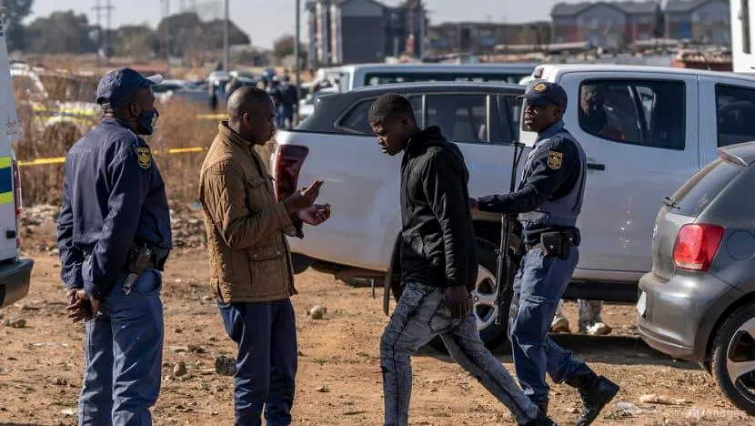 Cảnh sát dẫn một người đàn ông ra khỏi hiện trường vụ nổ súng tại quán bar ở Soweto, Nam Phi, ngày 10-7. Ảnh: AP