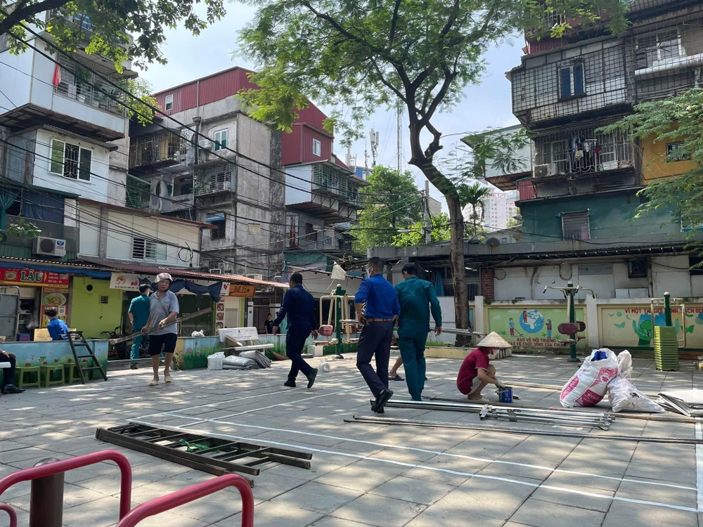 Lực lượng dân quân, tình nguyện viên chuẩn bị công tác dựng rạp trong sân nhà C3 khu tập thể Nghĩa Tân. Ảnh: NHƯ LOAN