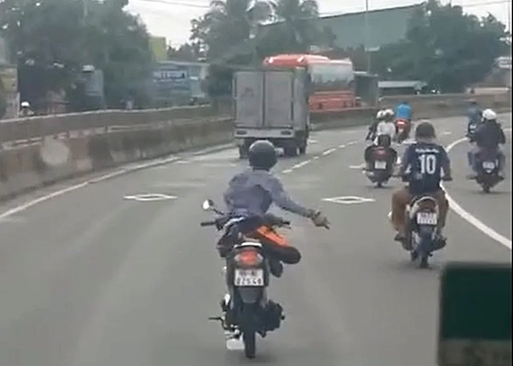 Thanh niên điều khiển xe máy bằng 1 tay, duỗi chân tay trước đầu ô tô. xe máy lạng lách