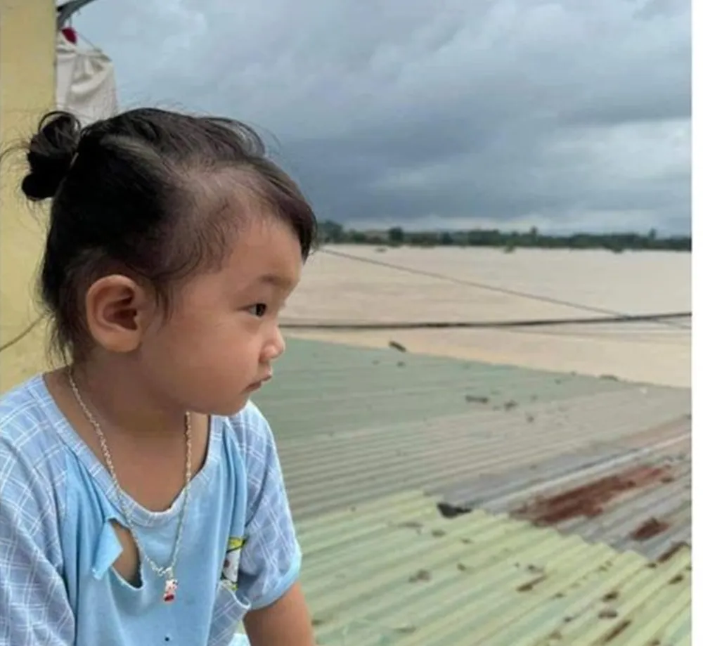 Một em bé ngồi trên nóc nhà trước cơn lũ lụt của bão số 3. bao-so-3 (1).jpg