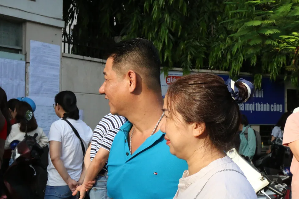 Anh Trương Tuấn Anh cùng vợ nhìn con bước vào điểm thi tại trường THPT Nguyễn Hữu Thọ. Ảnh: LONG VŨ 445874085_1192943815206511_887756863448358257_n.png
