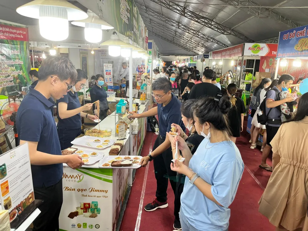 Nhân viên mời khách dùng thử bún gạo được chế biến ngay tại hội chợ vừa giới thiệu khuyến mãi mua 3 tặng 1