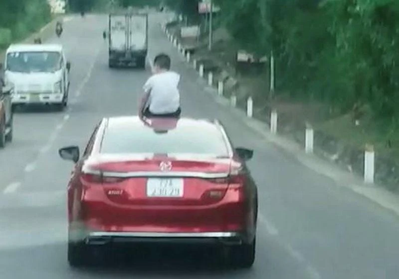 Bé trai ngồi trên mui ô tô khi xe đang chạy. Ảnh cắt từ clip Bé trai ngồi trên mui ô tô khi xe đang chạy. Ảnh cắt từ clip