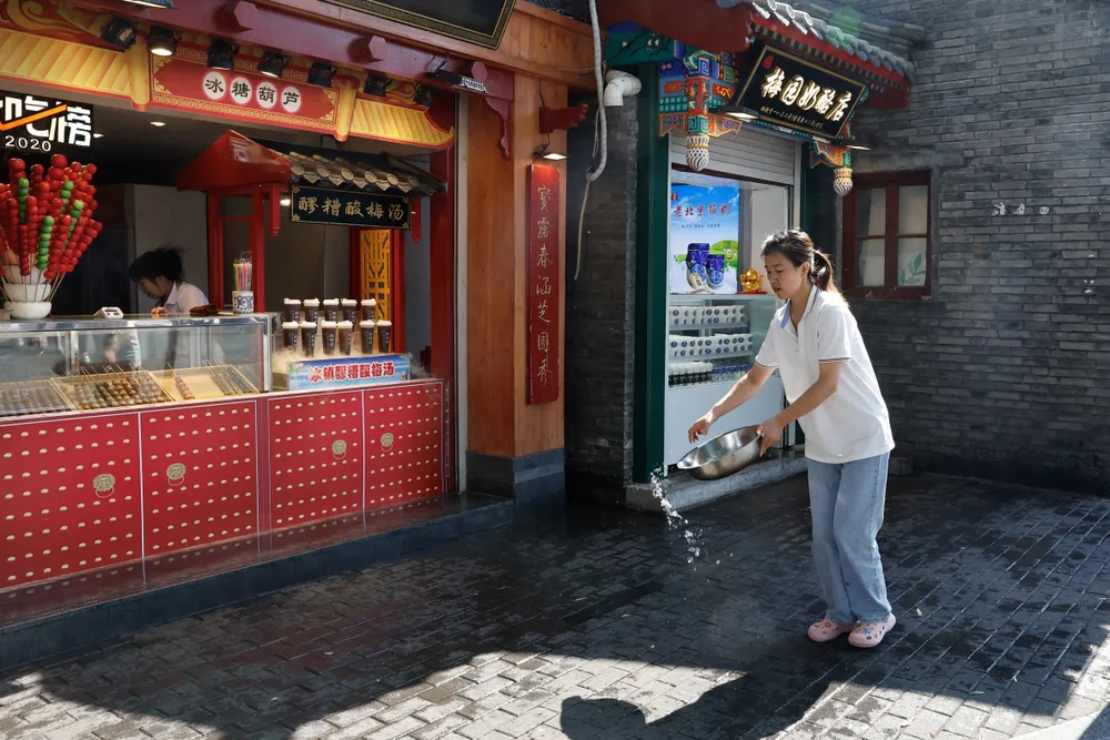 Một người bán hàng ở Bắc Kinh (Trung Quốc) dùng nước để hạ bớt nhiệt nhiệt độ trước cửa tiệm. Ảnh: REUTERS