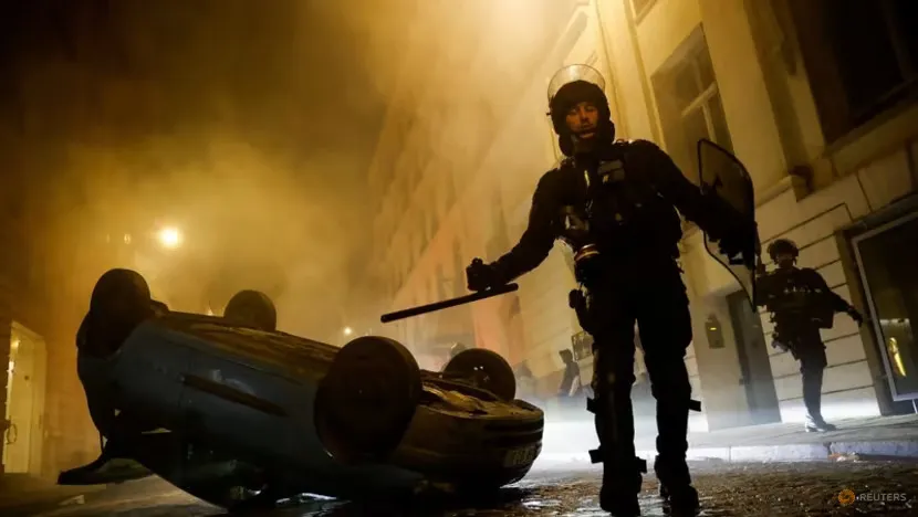 Cảnh sát chống bạo động Pháp bên cạnh một chiếc ô tô do người biểu tình phá hoại vào ngày 2-7. Ảnh: REUTERS Cảnh sát chống bạo động Pháp bên cạnh một chiếc ô tô do người biểu tình phá hoại vào ngày 2-7. Ảnh: REUTERS