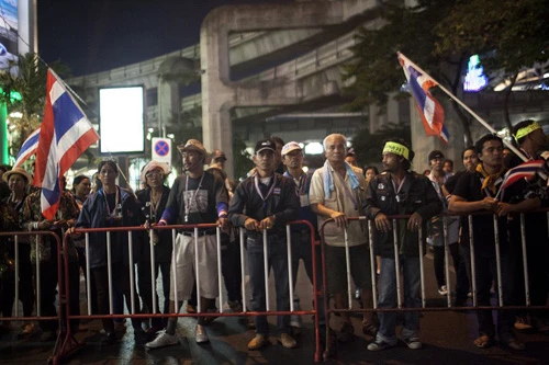 [Caption]Thai anti-government protesters hold national flags as they start massing behind a fence at one of their designated sites in a move to 'shut down' Bangkok on January 12, 2014.