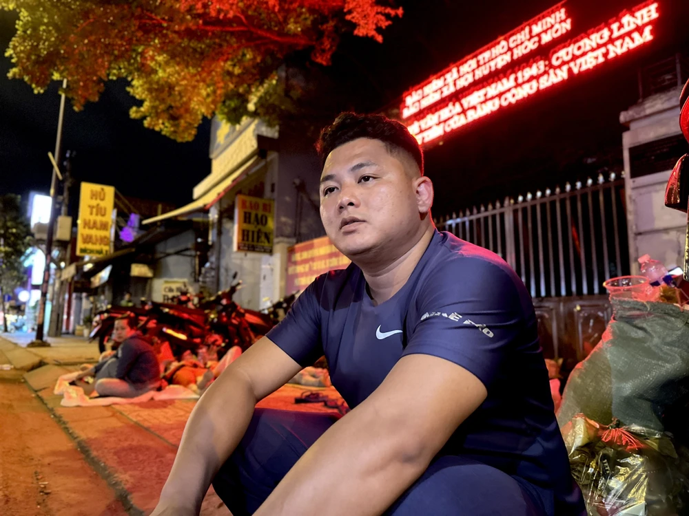 Anh Nguyễn Chí Hiếu ngồi một góc bên vỉa hè để vợ nằm nghỉ trên võng chờ đến 7 giờ 30 sáng để làm hồ sơ. Ảnh: TRẦN MINH